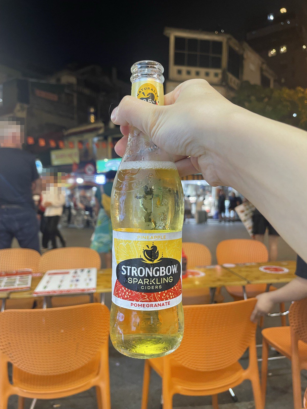 タヒエン通りでストロングボウのシードルの瓶を持つ手。オレンジのイスが並ぶ