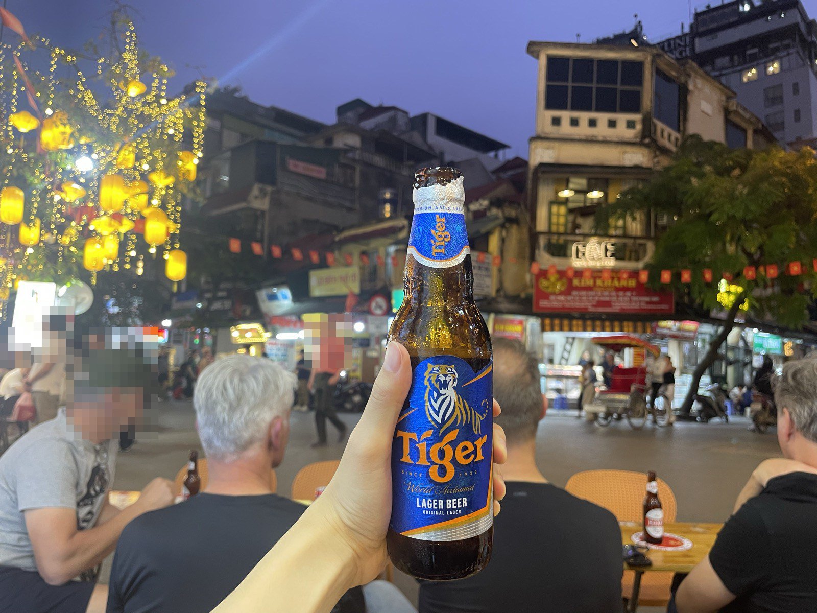タヒエン通りの路上席でタイガービールの瓶を持つ手。奥に旧市街の街並み